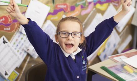 Excited child with arms raised in classroom