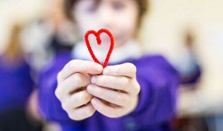 Blurred child in background holding in focus red heart in foreground