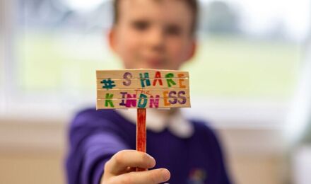 Child blurred in background, sign in foreground reading 'share the kindness'
