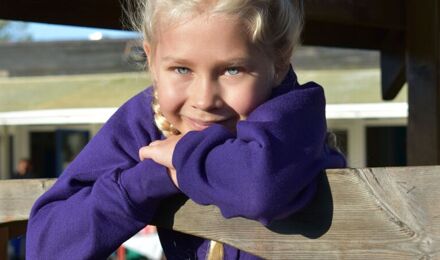 Child with crossed arms leaning on  play equipment smiling to camera