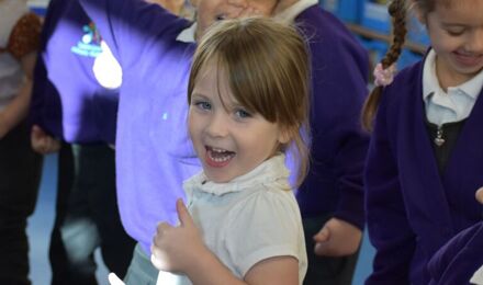 Smiling child giving a thumbs up in a crowd