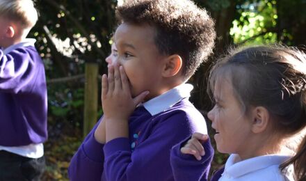 Child covering mouth in amazement in forest school